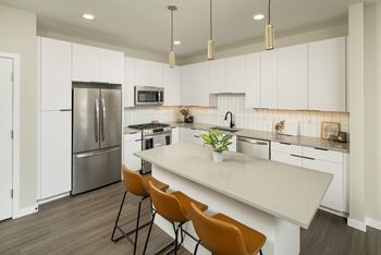 A kitchen with a refrigerator, microwave, and a counter with chairs.